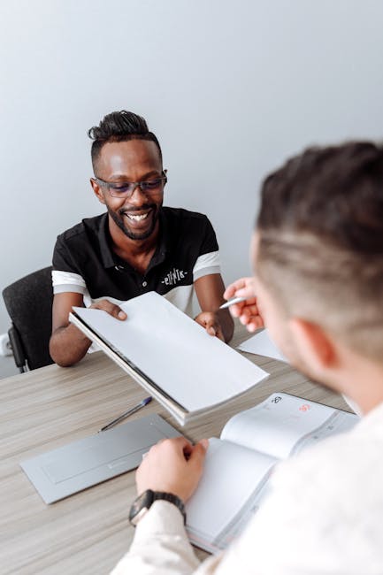 Two colleagues engage in a discussion during an office meeting, sharing documents and ideas.